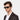 A man with refined features wears Oak Black Green Sunglasses with confidence. His tailored blazer and crisp white shirt enhance the timeless elegance of the frame, making it the focal point of a modern, understated look. TBD Eyewear handmade in Italy from sustainable materials.