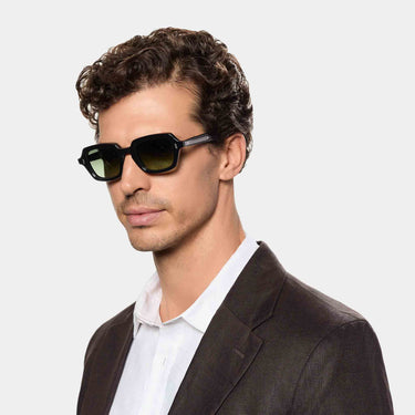 A man with refined features wears Oak Black Green Sunglasses with confidence. His tailored blazer and crisp white shirt enhance the timeless elegance of the frame, making it the focal point of a modern, understated look. TBD Eyewear handmade in Italy from sustainable materials.